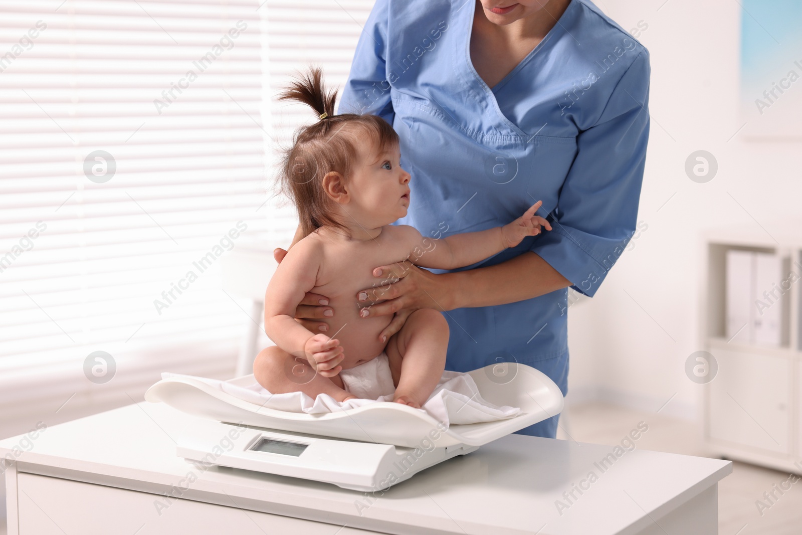 Photo of Pediatrician weighting cute little girl in clinic. Checking baby's health