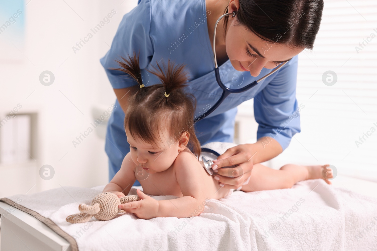 Photo of Pediatrician examining cute little girl with stethoscope in clinic. Checking baby's health