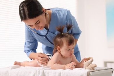 Photo of Pediatrician examining cute little girl with stethoscope in clinic. Checking baby's health