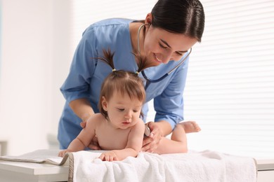 Photo of Pediatrician examining cute little girl with stethoscope in clinic. Checking baby's health