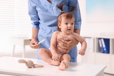 Photo of Pediatrician examining cute little girl with thermometer in clinic, closeup. Checking baby's health