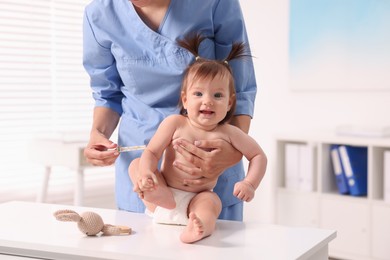 Photo of Pediatrician examining cute little girl with thermometer in clinic, closeup. Checking baby's health