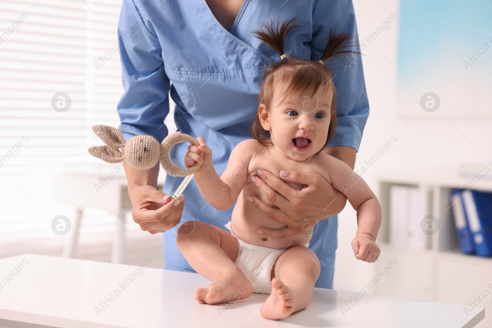 Photo of Pediatrician examining cute little girl with thermometer in clinic, closeup. Checking baby's health