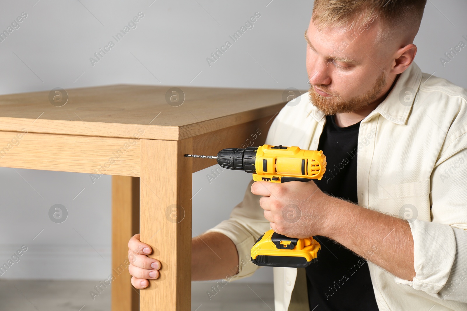 Photo of Man with electric screwdriver assembling table indoors