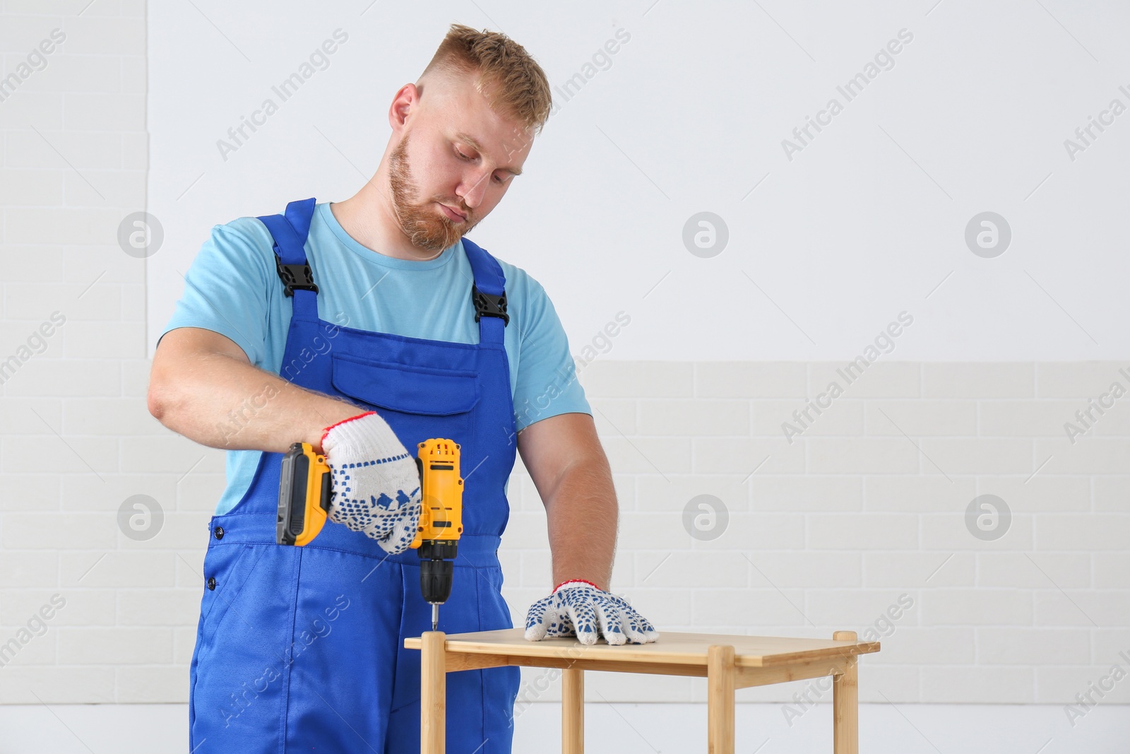 Photo of Worker with electric screwdriver assembling furniture indoors. Space for text