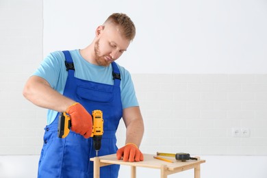 Photo of Worker with electric screwdriver assembling furniture indoors. Space for text