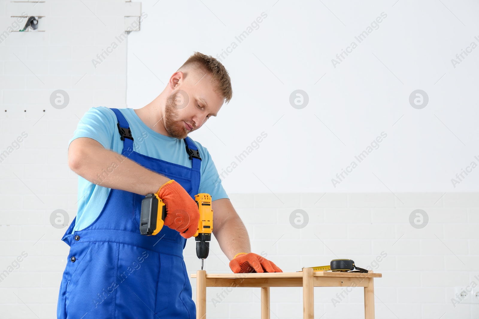 Photo of Worker with electric screwdriver assembling furniture indoors. Space for text