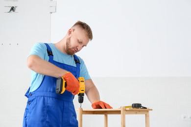 Photo of Worker with electric screwdriver assembling furniture indoors. Space for text