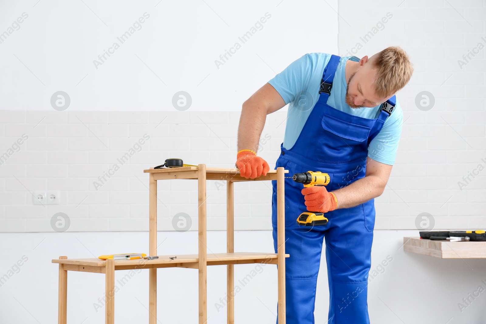 Photo of Worker with electric screwdriver assembling furniture indoors