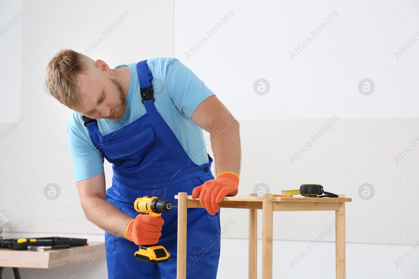 Photo of Worker with electric screwdriver assembling furniture indoors