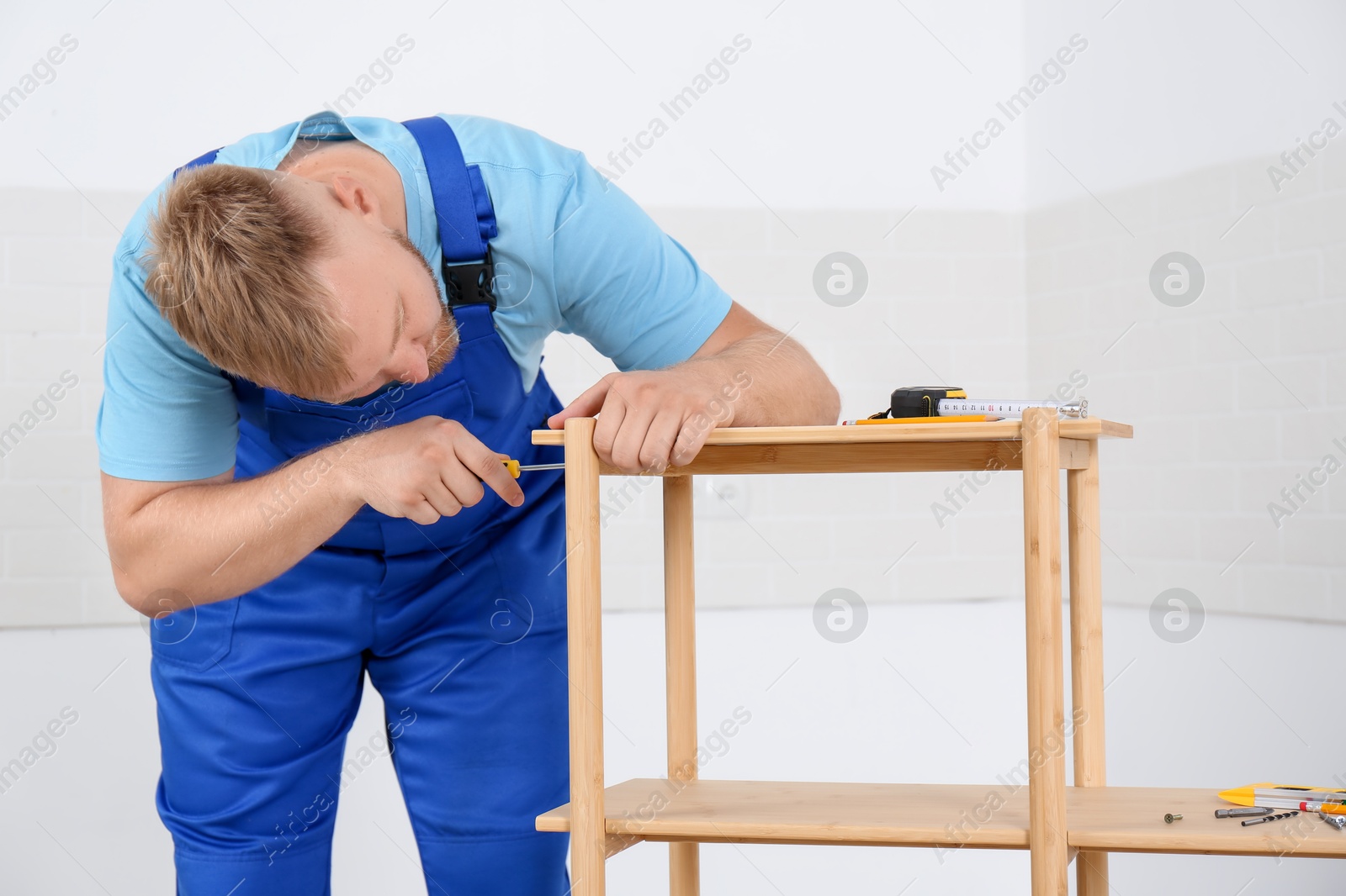 Photo of Worker with screwdriver assembling wooden furniture indoors