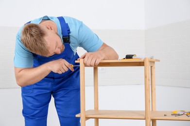 Worker with screwdriver assembling wooden furniture indoors