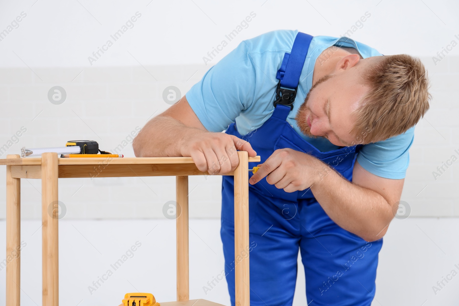 Photo of Worker with screwdriver assembling wooden furniture indoors