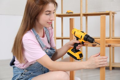 Photo of Woman with electric screwdriver assembling furniture indoors