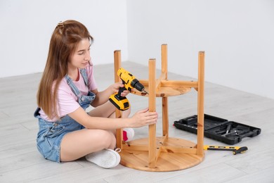 Photo of Woman with electric screwdriver assembling table on floor at home