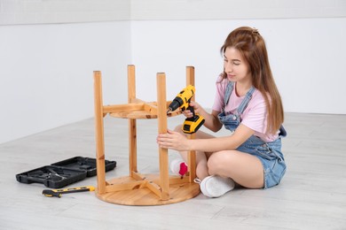 Woman with electric screwdriver assembling table on floor at home