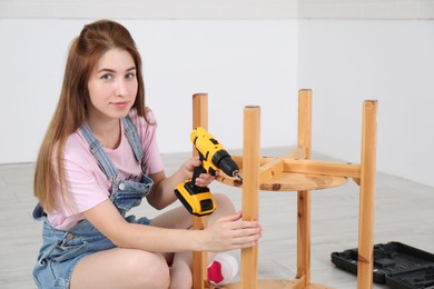 Photo of Woman with electric screwdriver assembling furniture indoors