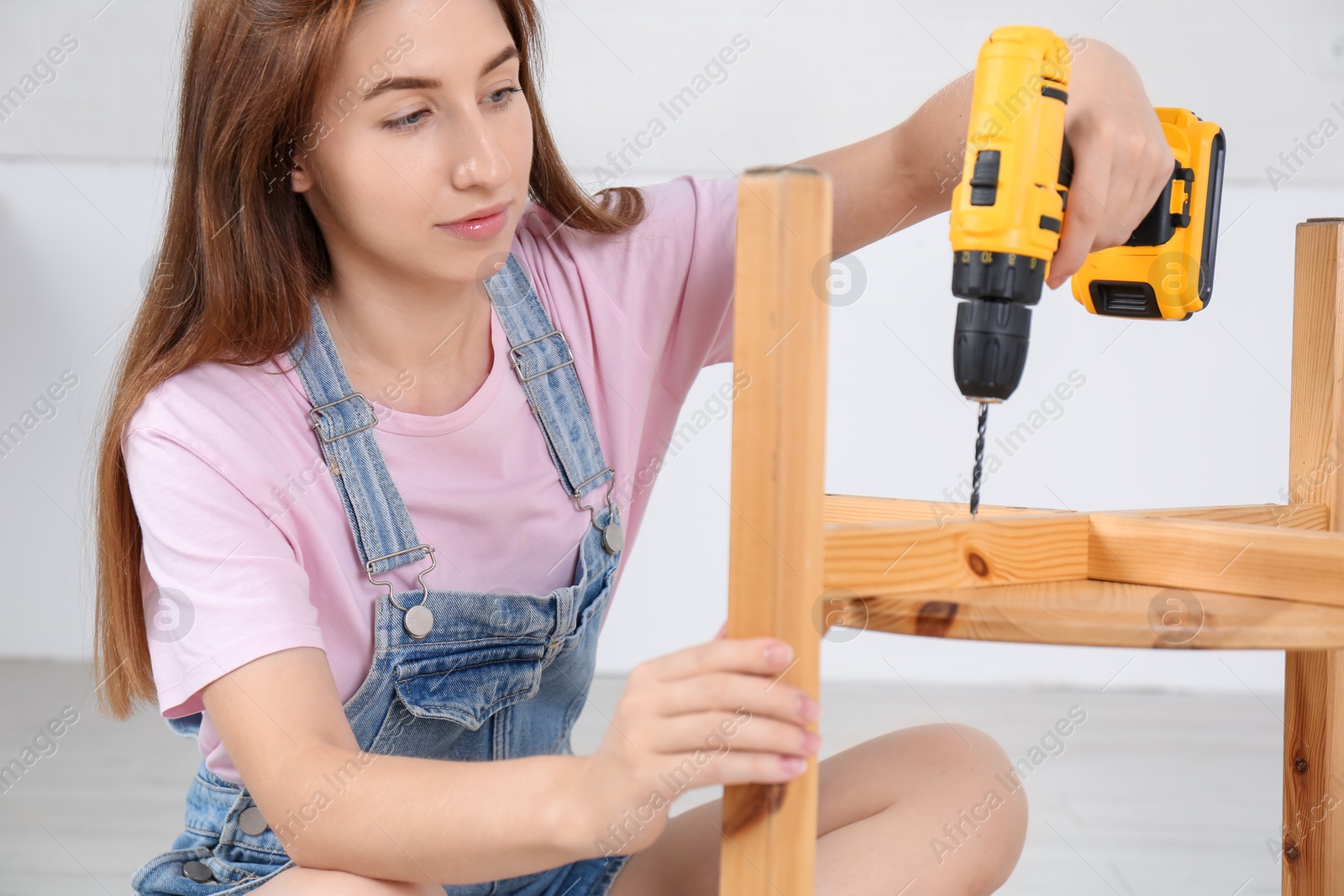 Photo of Woman with electric screwdriver assembling furniture indoors