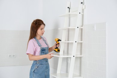 Woman with electric screwdriver assembling ladder shelf indoors