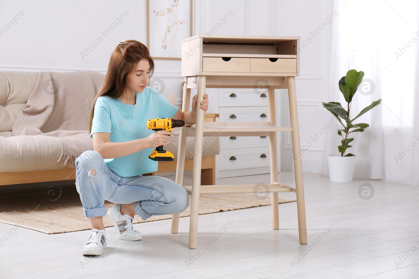 Photo of Woman with electric screwdriver assembling table in room