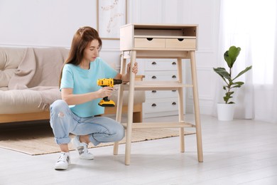 Woman with electric screwdriver assembling table in room