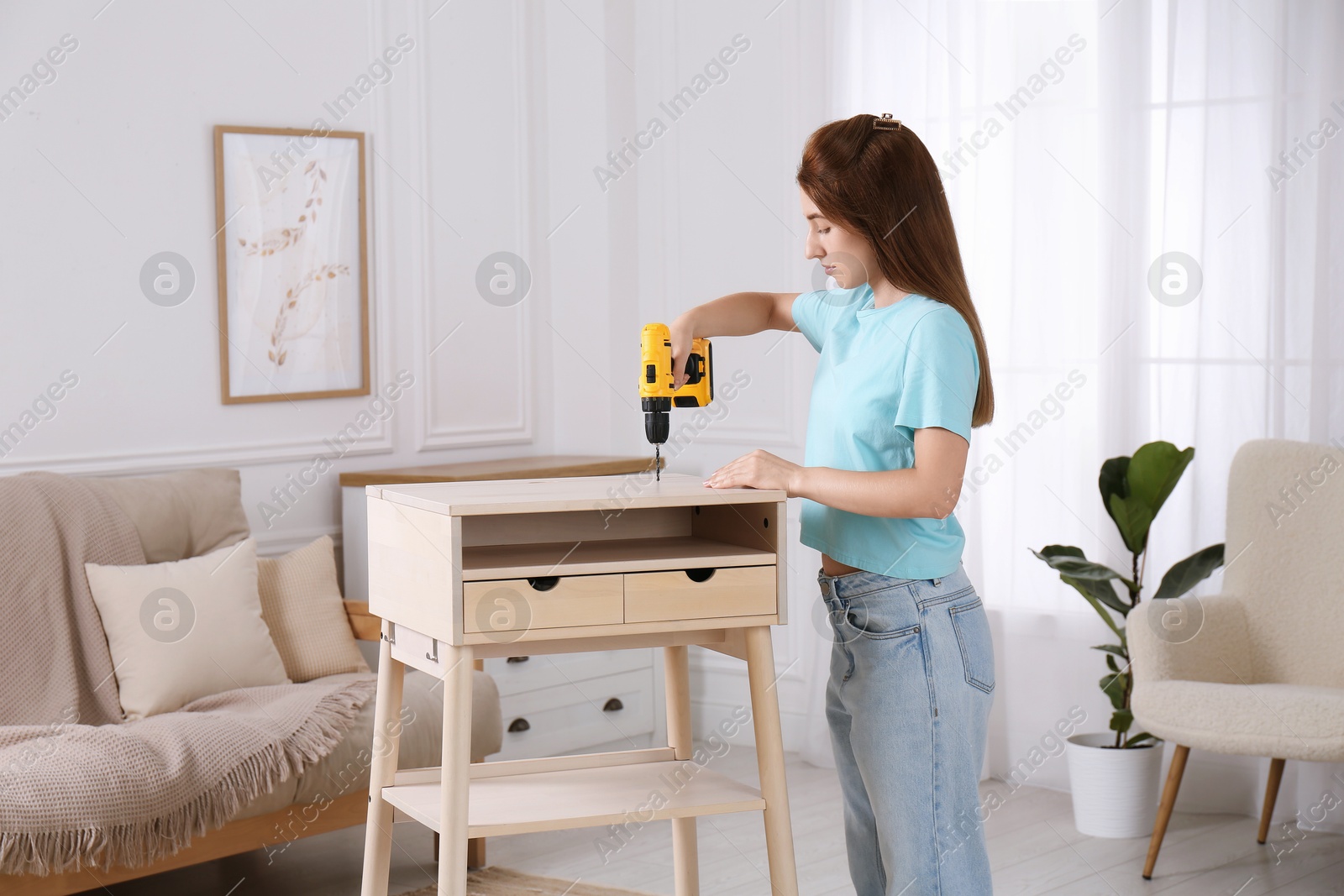 Photo of Woman with electric screwdriver assembling table in room