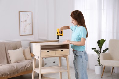 Woman with electric screwdriver assembling table in room