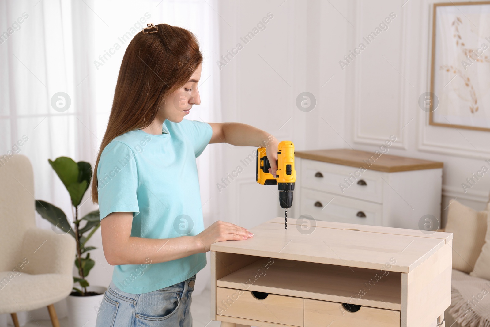 Photo of Woman with electric screwdriver assembling table in room