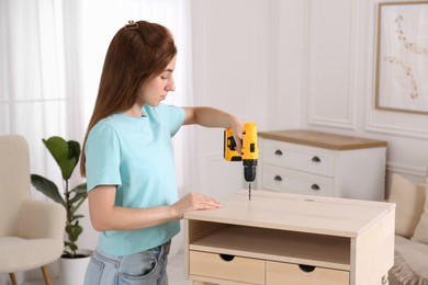 Woman with electric screwdriver assembling table in room