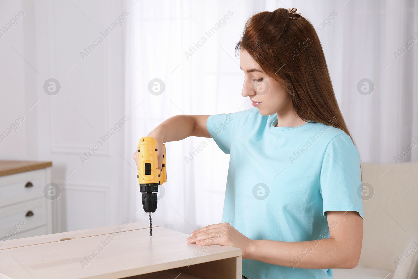 Photo of Woman with electric screwdriver assembling furniture at home