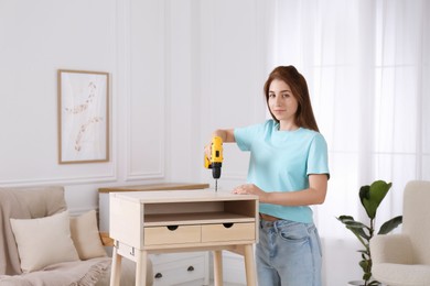 Photo of Woman with electric screwdriver assembling table in room