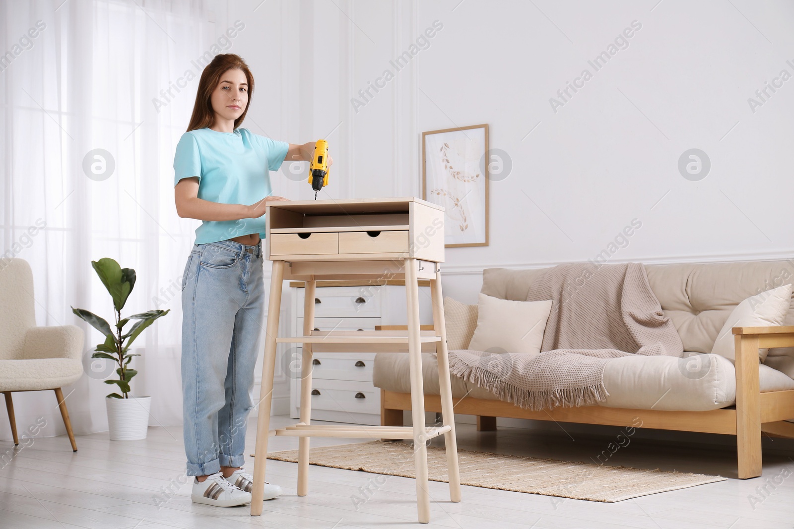 Photo of Woman with electric screwdriver assembling table in room