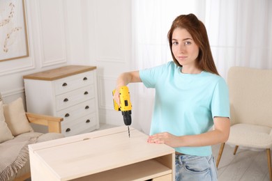 Woman with electric screwdriver assembling table in room