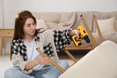 Woman with electric screwdriver assembling armchair at home