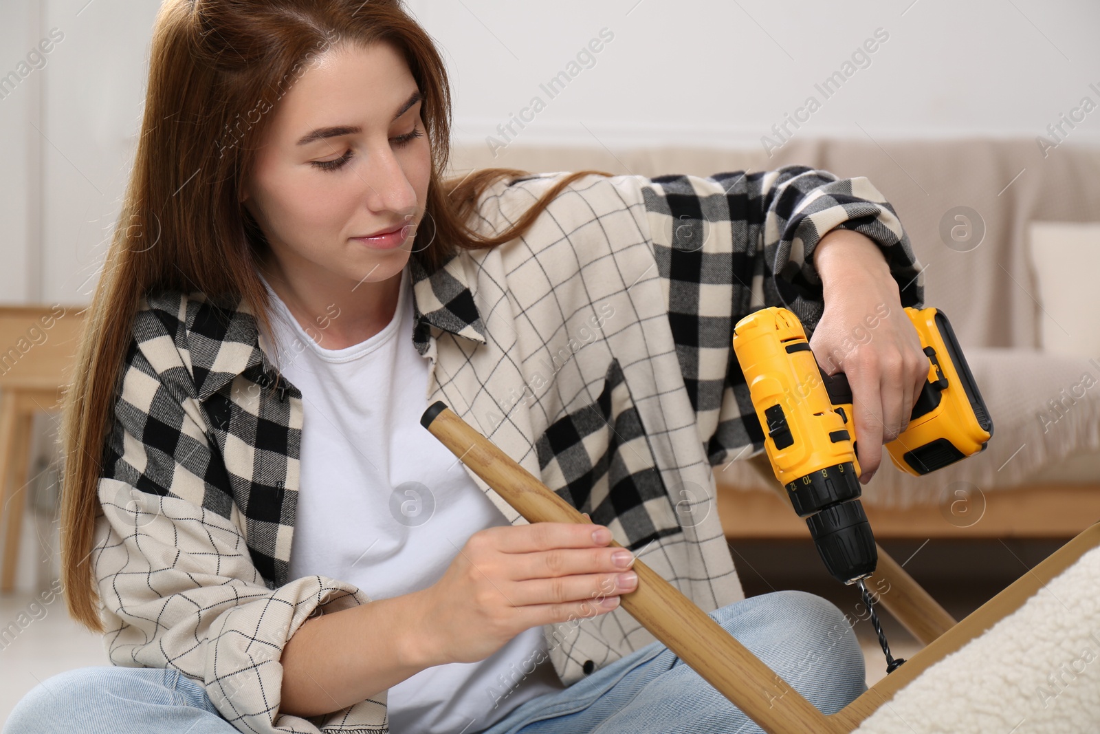 Photo of Woman with electric screwdriver assembling armchair at home