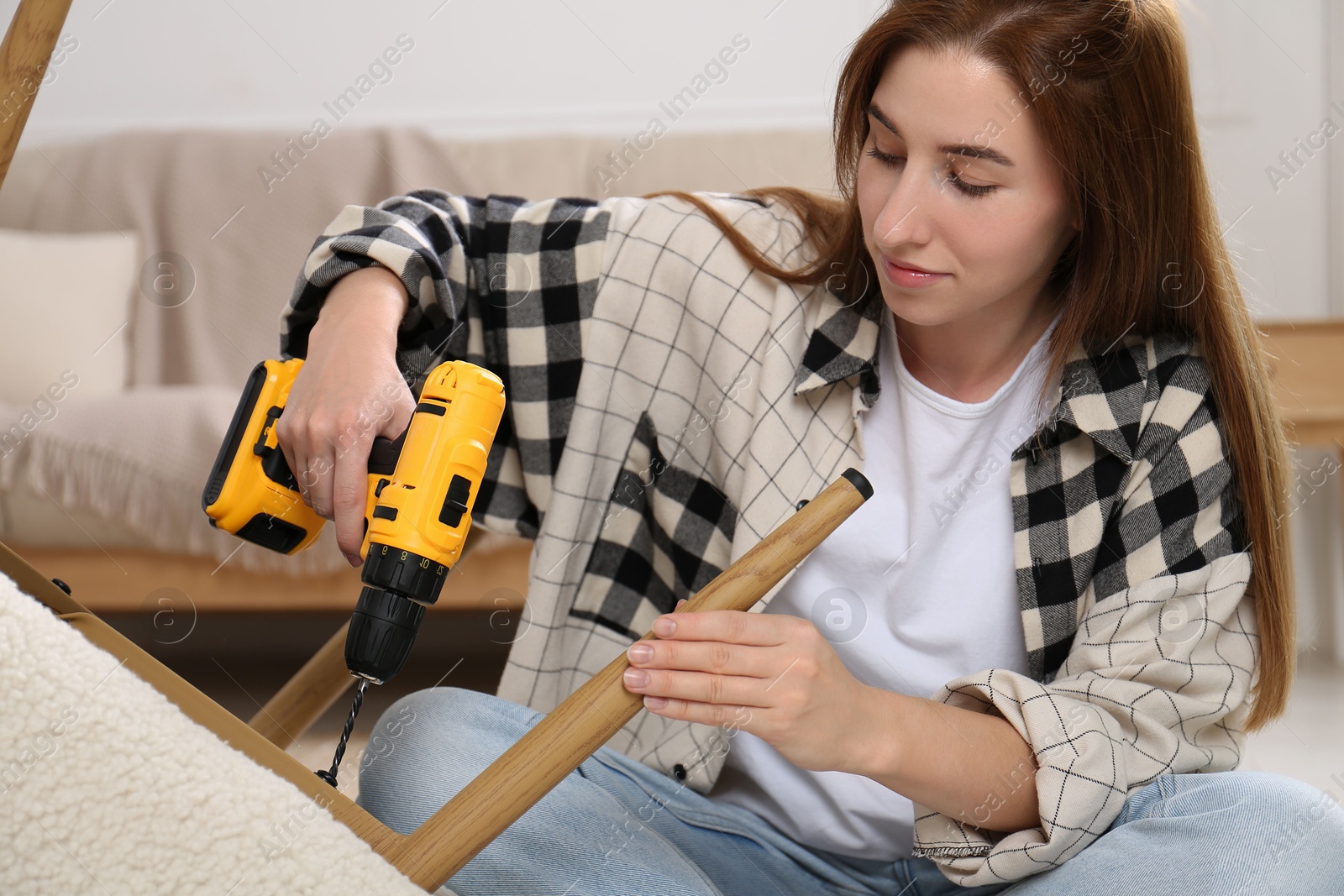 Photo of Woman with electric screwdriver assembling armchair at home