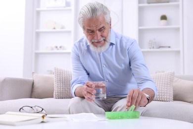 Senior man with glass of water taking pill from organizer at home