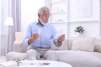 Photo of Senior man with pills reading medicine instruction at home