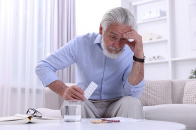 Senior man with pills on sofa at home