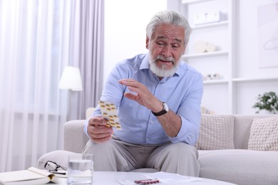 Senior man with pills on sofa at home