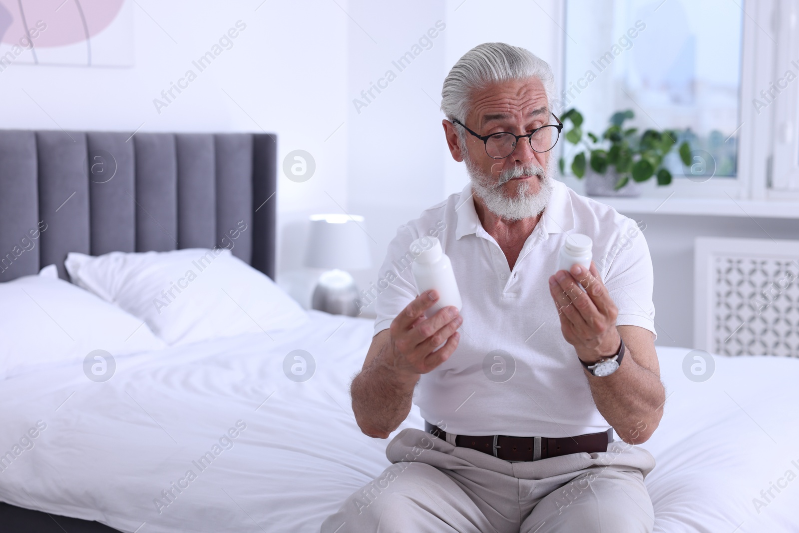 Photo of Senior man with bottles of pills on bed indoors, space for text