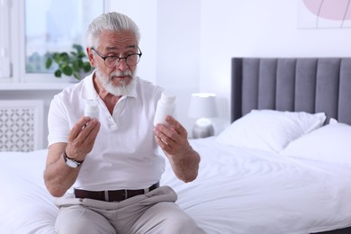 Photo of Senior man with bottles of pills on bed indoors, space for text