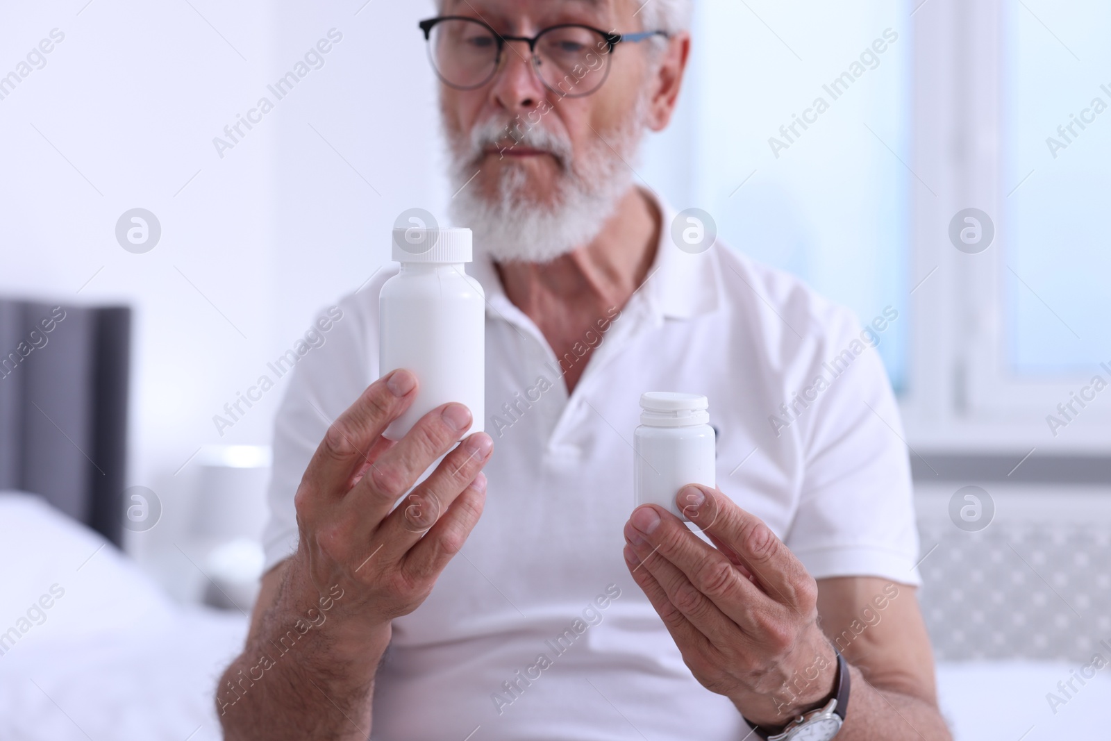 Photo of Senior man with bottles of pills indoors, selective focus