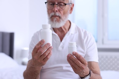 Senior man with bottles of pills indoors, selective focus