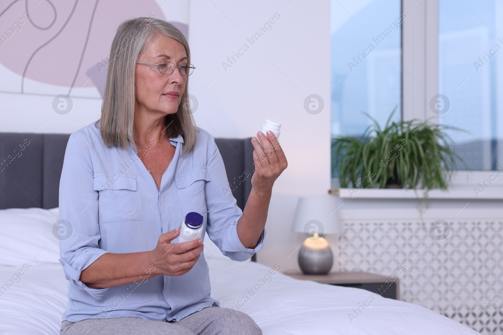 Photo of Senior woman with bottles of pills on bed indoors