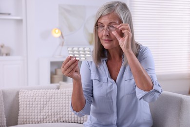 Senior woman holding blister with pills at home