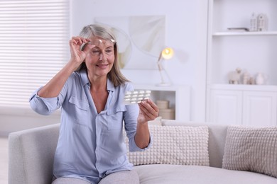 Senior woman holding blister with pills at home