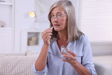 Senior woman with glass of water taking pill at home