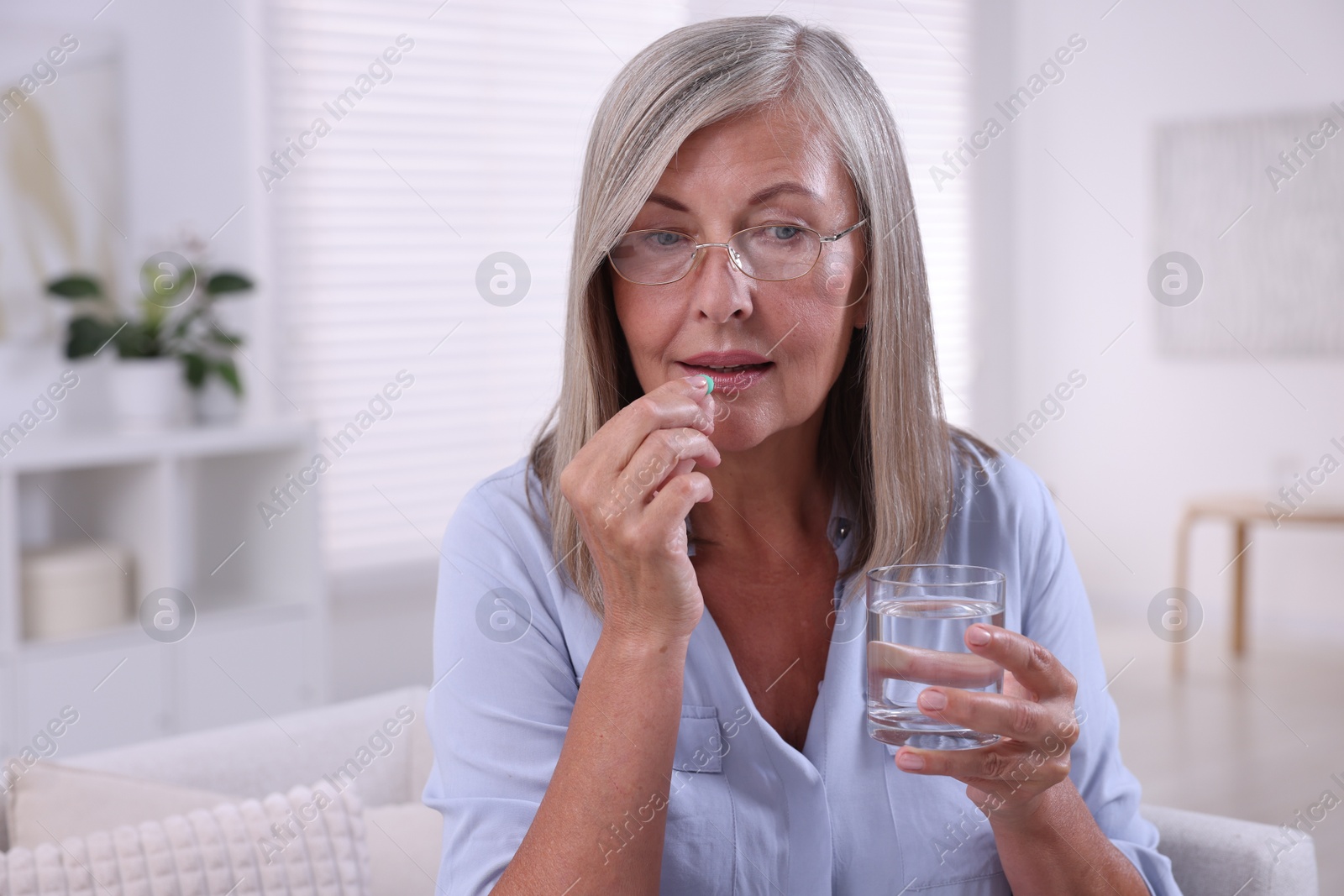 Photo of Senior woman with glass of water taking pill at home, space for text