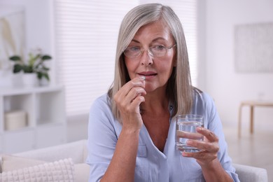 Photo of Senior woman with glass of water taking pill at home, space for text